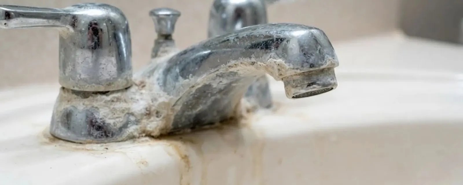 Chrome bathroom faucet crusted with white and tan mineral scale from hard water