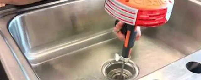 Hand-crank drain auger being fed into a stainless steel kitchen sink drain