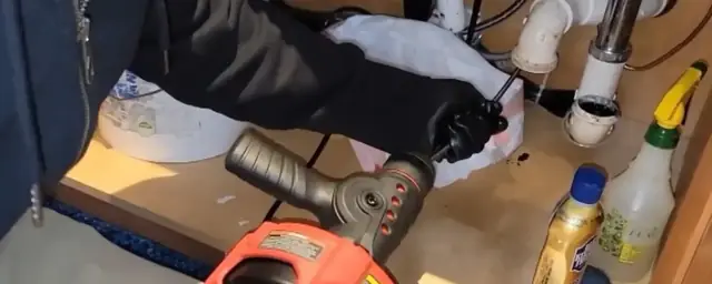 Hands feeding a drain cable machine through the P-trap area under a kitchen sink