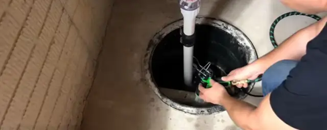 Person lowering a pump into a sump basin with the discharge pipe running up through the lid