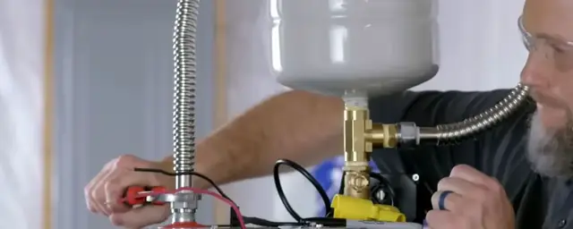 Plumber fitting an expansion tank and brass tee on top of a new water heater